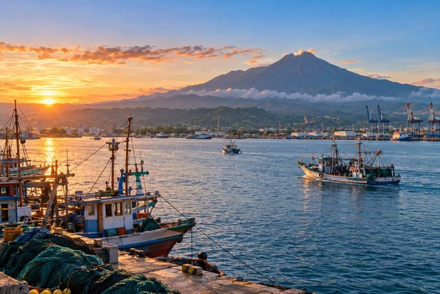 Illustration of working fishing boats on a broad bay with green lowlands beyond General Santos