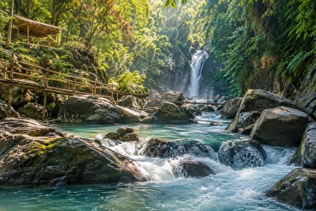 Illustration of a lush river gorge with smooth boulders, clear water, and bamboo footbridges in Tibiao, Antique
